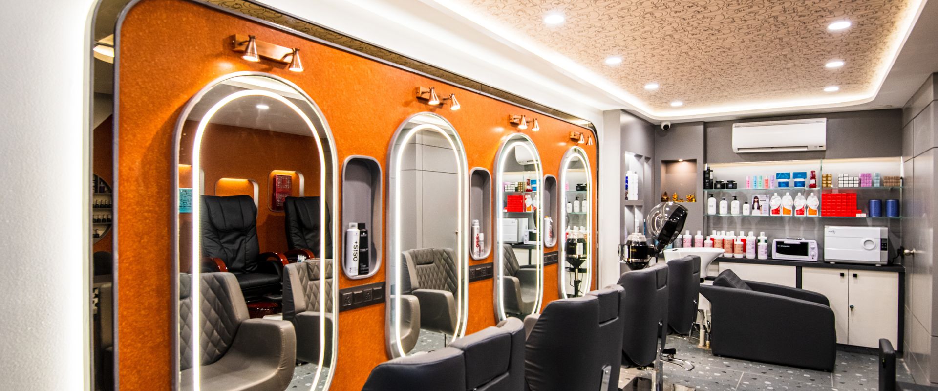 The styling floor at Ftry Salon: a row of lit oval mirrors on an orange feature wall, with styling chairs facing them.